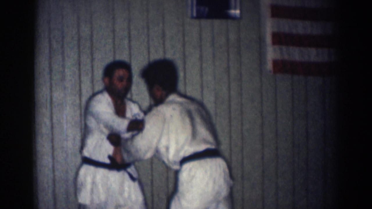 Two men in white gi practice a standing grip or setup during a 1966 indoor karate session in San Gabriel.