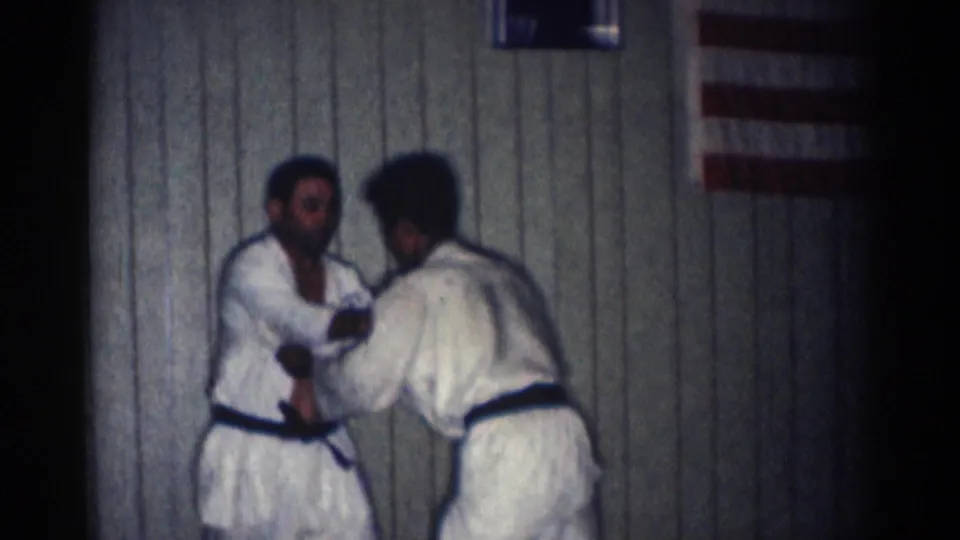 Two men in white gi practice a standing grip or setup during a 1966 indoor karate session in San Gabriel.
