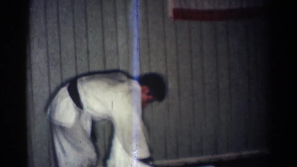 A karate practitioner in a white gi bends near the wood-paneled wall during the brief 1966 San Gabriel practice footage.