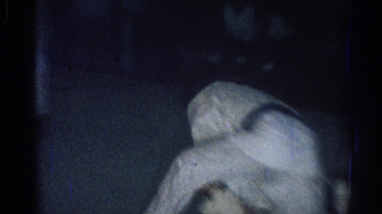 Two adults in white gi grapple low on a dark mat in a dimly lit room.