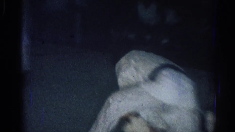 Two adult martial arts practitioners in white gi are locked in a low grappling position on the mat in the San Gabriel home-movie clip.