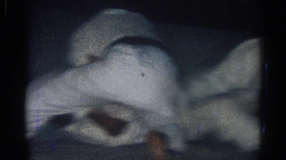 A tight, grainy 8mm frame shows white gi fabric and limbs during a close grappling maneuver on the dark mat.