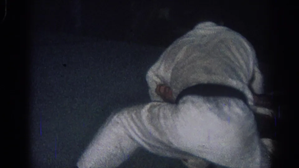 An adult martial arts practitioner in a white gi bends forward on the mat during the final moments of the 1966 indoor practice clip.