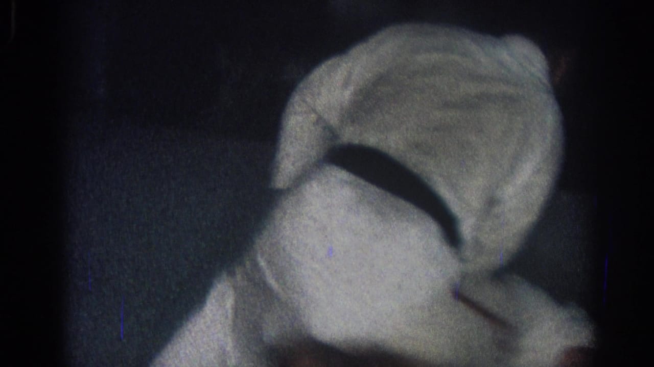 Two gi-clad martial arts practitioners grapple on a dark mat in low light.