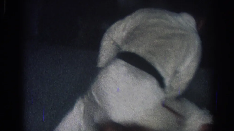 1966 San Gabriel home-movie frame showing two people in white gi uniforms locked in a close ground exchange on a dark mat.