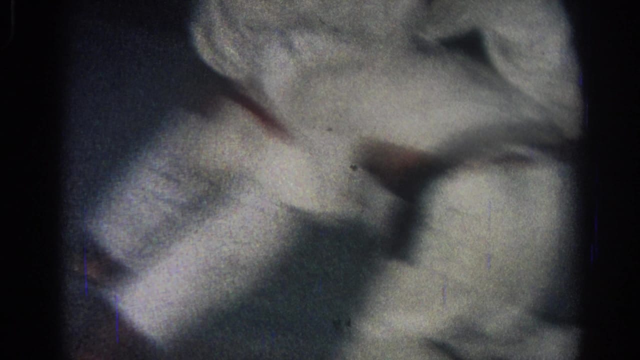 Close 8mm frame from the San Gabriel clip showing white gi fabric and limbs compressed during a martial arts ground hold.