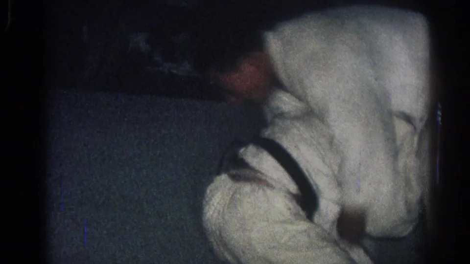 1966 8mm frame showing a martial arts participant leaning over another person during a low-light ground struggle.