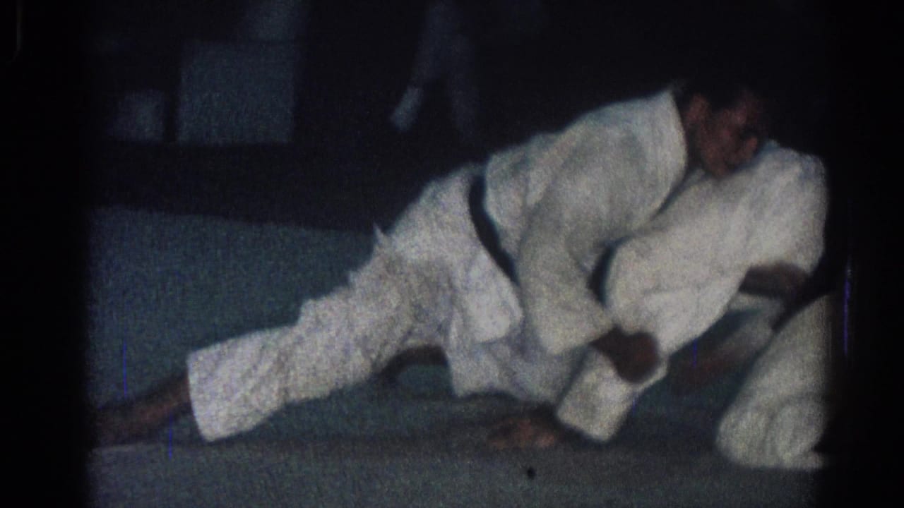 Two men in white judo uniforms grapple low on a dark mat.