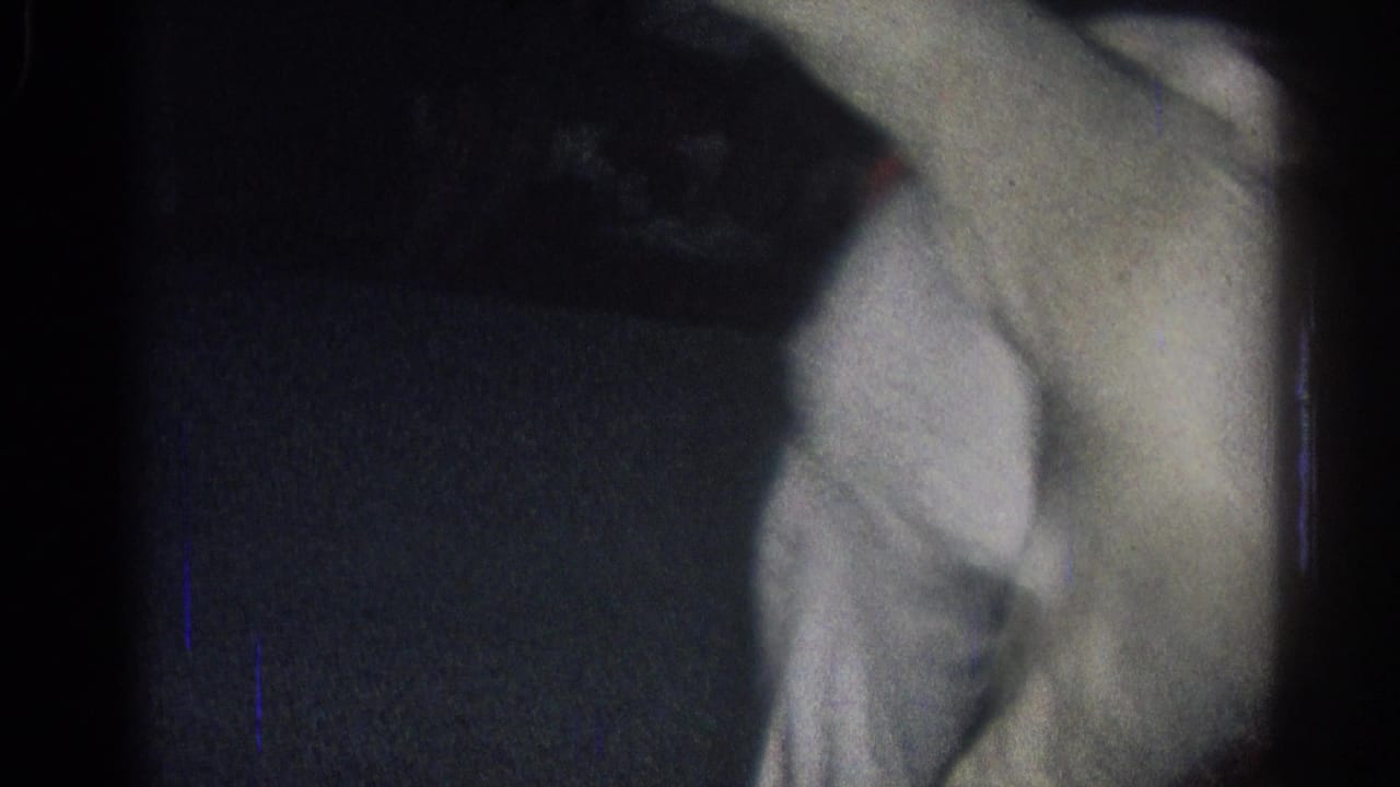 A judo practitioner in a white gi moves across the mat in low light.