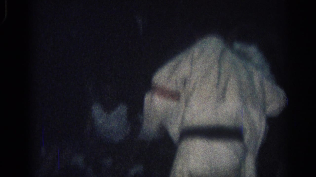 A dim 1966 San Gabriel frame shows a martial arts participant in a white gi bent forward, with another figure partly obscured nearby.