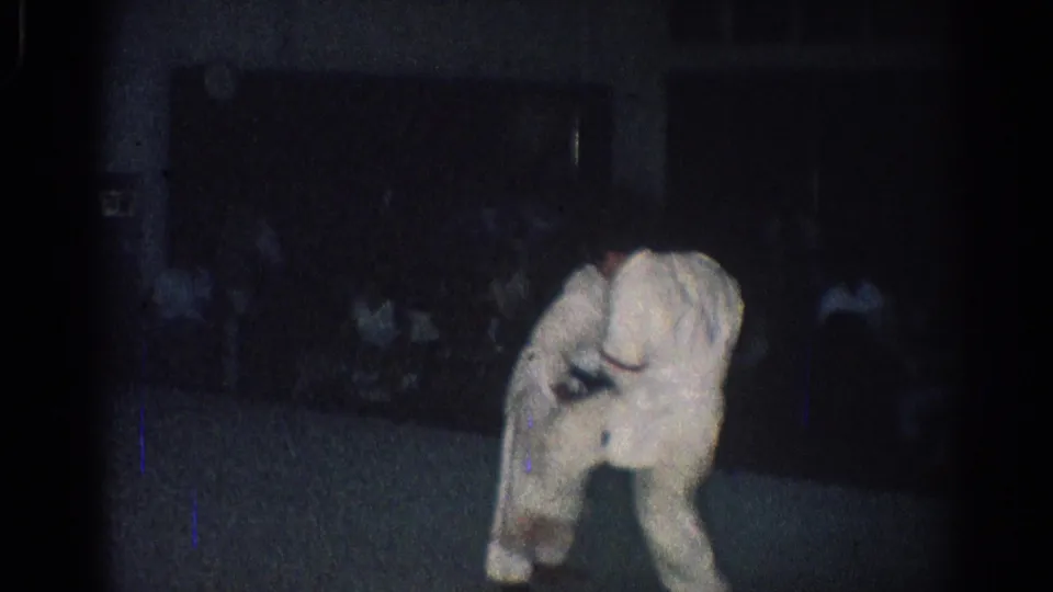 In this San Gabriel 1966 frame, a martial arts participant bends near the floor while spectators are faintly visible in the background.