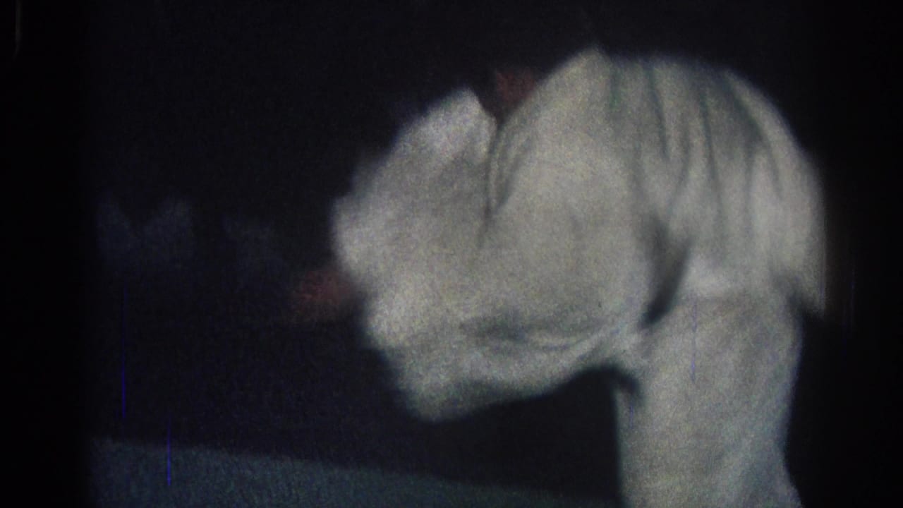 Two martial artists in white gi bend forward during a dimly lit judo practice scene.