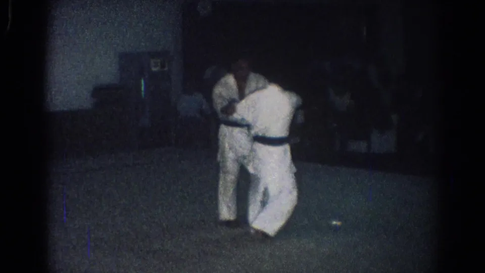 A wider 1966 San Gabriel frame shows two judo practitioners in white gi locked together on a mat-like floor in a shadowed indoor space.