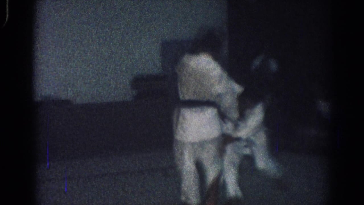 Two judo practitioners in white gi grapple in a dim indoor room.