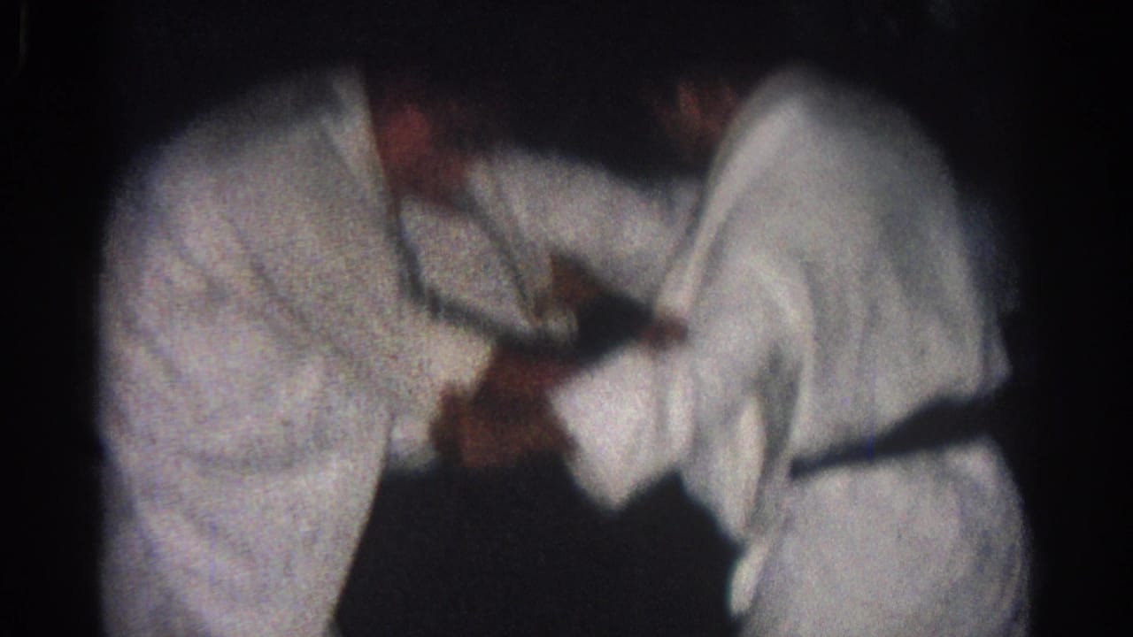 Two men in white judo gis grip each other on a dark mat.