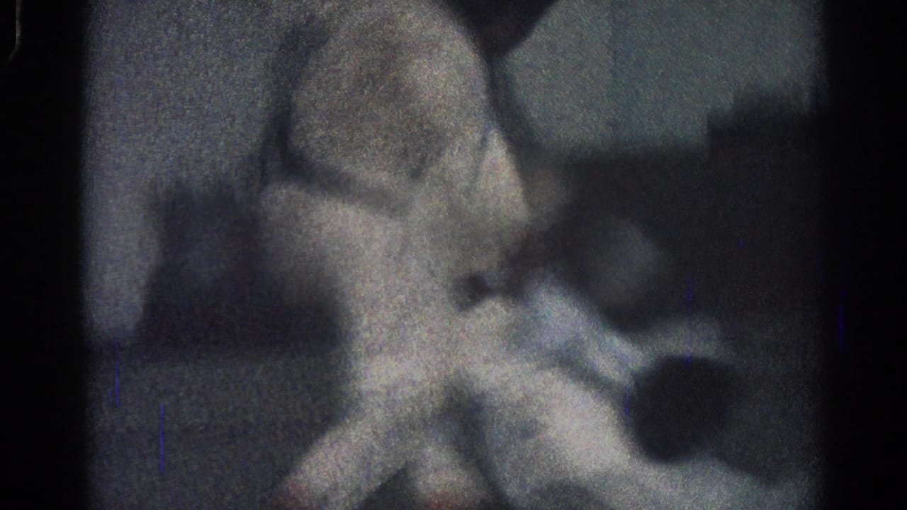 Two people in white uniforms grapple on a dark indoor floor in a grainy frame.