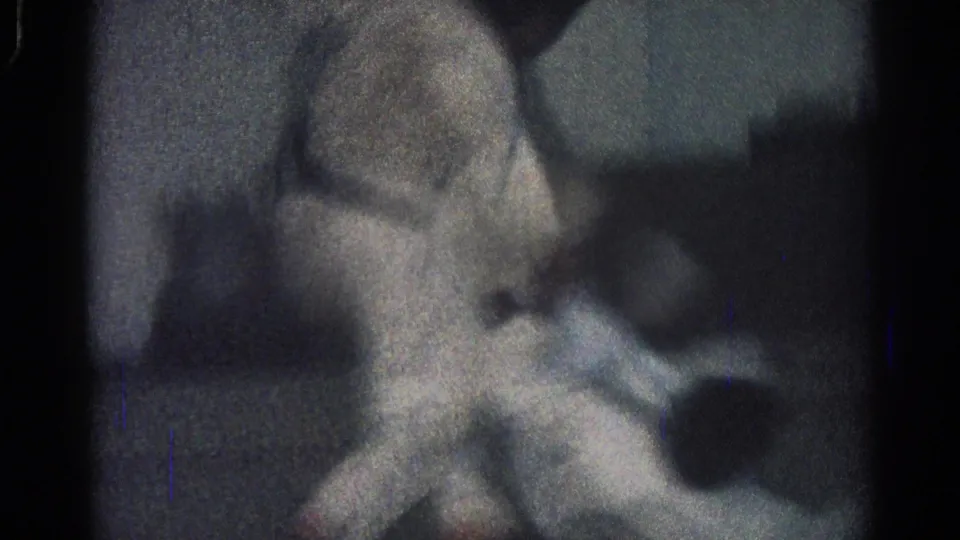 1966 San Gabriel 8mm frame showing two martial arts practitioners in white uniforms engaged in close floor grappling under dim light.