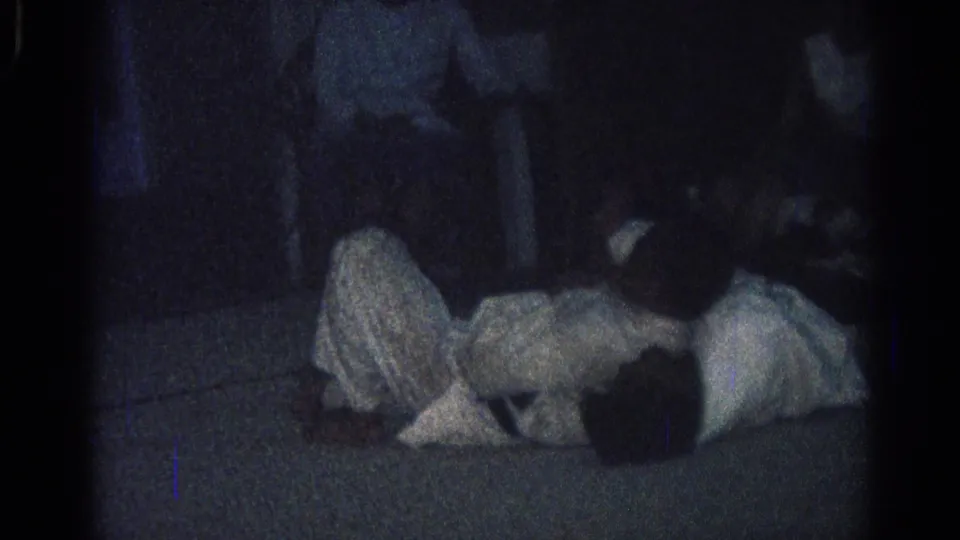 1966 San Gabriel home-movie frame showing two martial arts practitioners in white uniforms working through a ground technique.