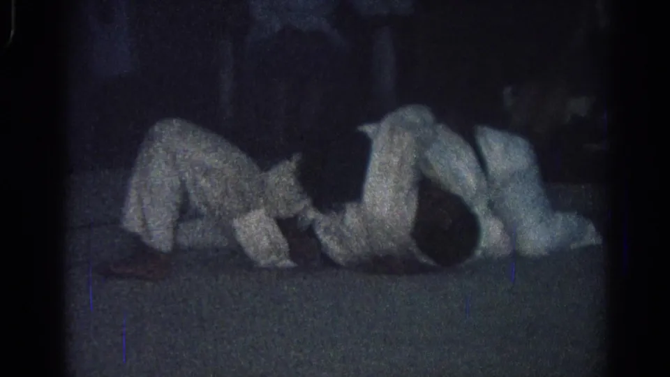 1966 San Gabriel 8mm frame of two martial arts practitioners in white uniforms completing a floor-based grappling movement.