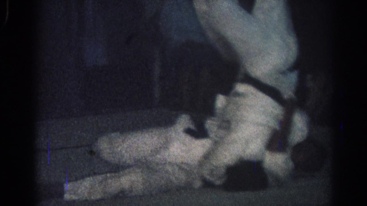 San Gabriel, California 1966 frame showing one man in a white uniform down on the mat while another leans over during a close grapple.