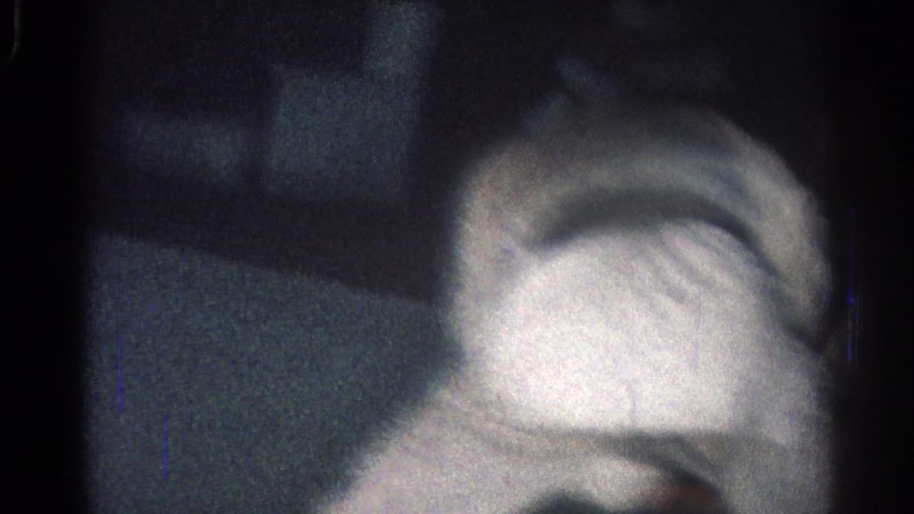 A martial artist in a white gi bends low during a close grappling movement, partly obscured by darkness.