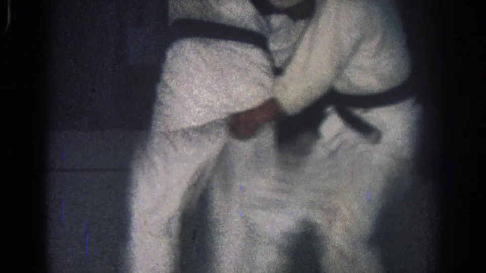 1966 San Gabriel home-movie frame showing two black-belt martial artists in white gi during a tight grappling hold near the end of the clip.