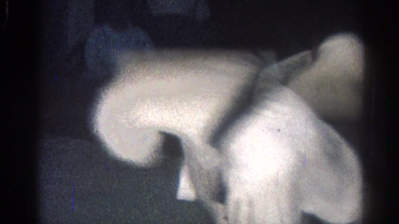 Two people in white gi uniforms grapple low on a dark mat.