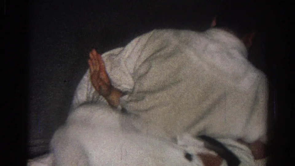1966 San Gabriel home-movie frame shows a gi-clad participant leaning over another person in a close dojo grappling position.