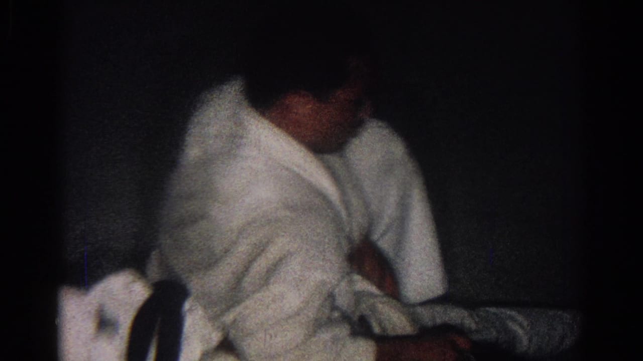 Two martial artists in white uniforms grapple on a dark floor.