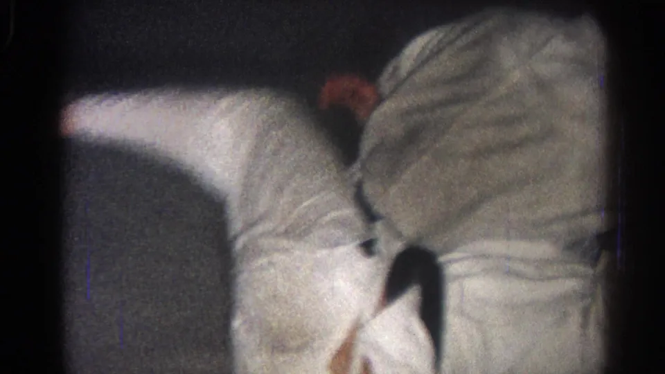 Two martial artists in white gi continue ground work in the dim San Gabriel home-movie footage from 1966.