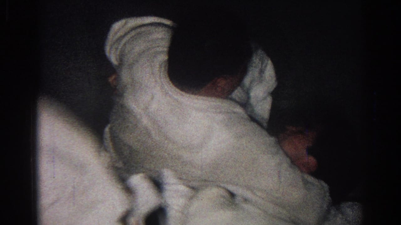 Two athletes in white gis grappling on a dark mat in low light.
