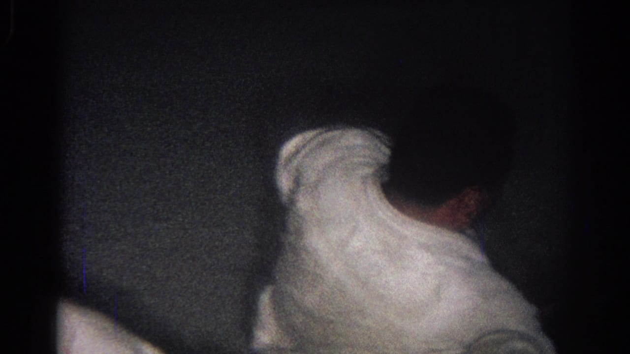 A judo athlete in a white gi bends forward on a dark mat.