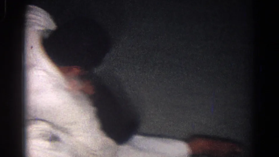 1966 San Gabriel home-movie frame with judo athletes partly obscured as they continue grappling on a dark training mat.
