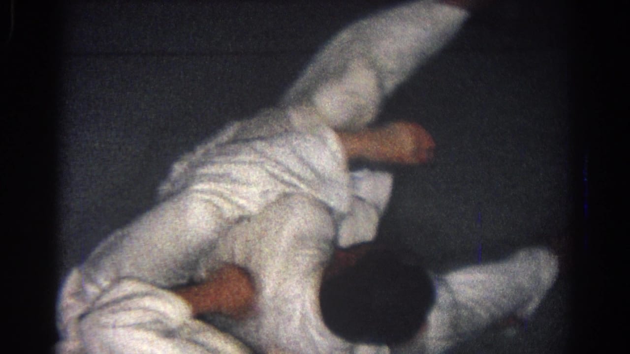 Two men in white gi uniforms grapple on a dark mat.