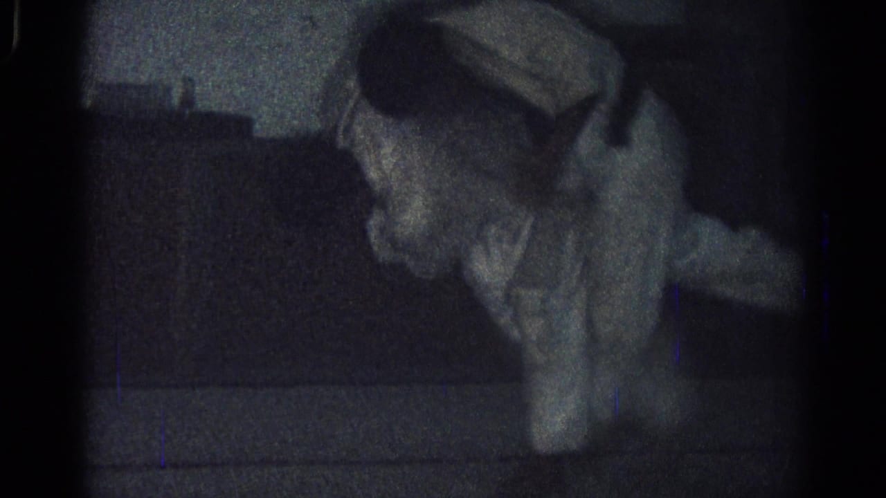 A man in a white gi is bent forward near the floor in a dim interior.