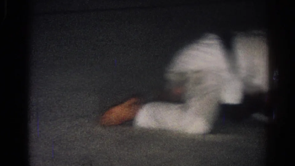 A white-uniformed adult competitor is down on the dark mat during the San Gabriel martial arts match.