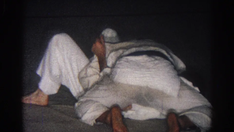 A competitor sits partly upright while another remains low in a white uniform during the San Gabriel martial arts match.