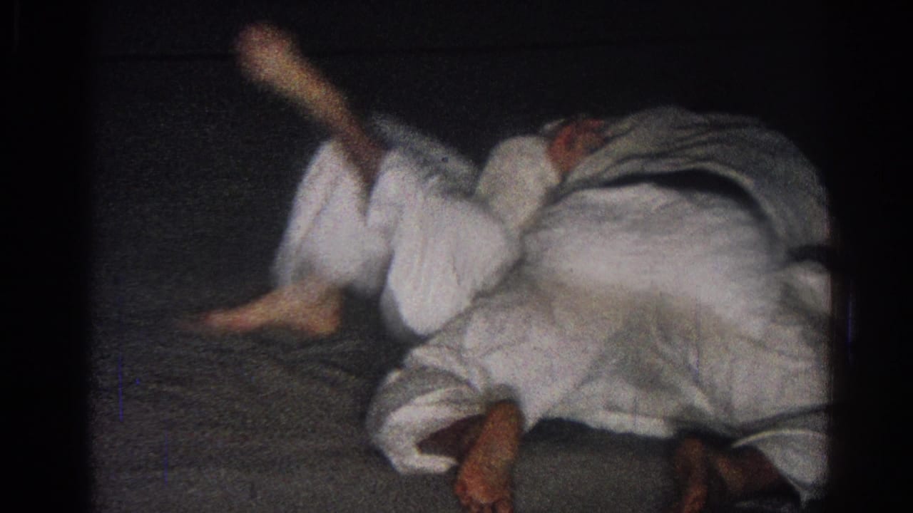 1966 San Gabriel 8mm frame showing two men in white martial arts uniforms grappling low on a dark indoor mat.