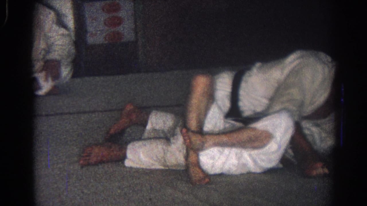 A judo student bends over another student lying on the mat during practice.