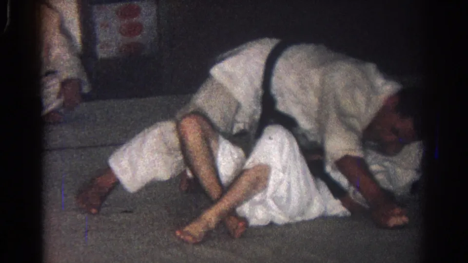 1966 San Gabriel 8mm frame with two martial artists in white gi engaged in a low judo hold on a gray mat.