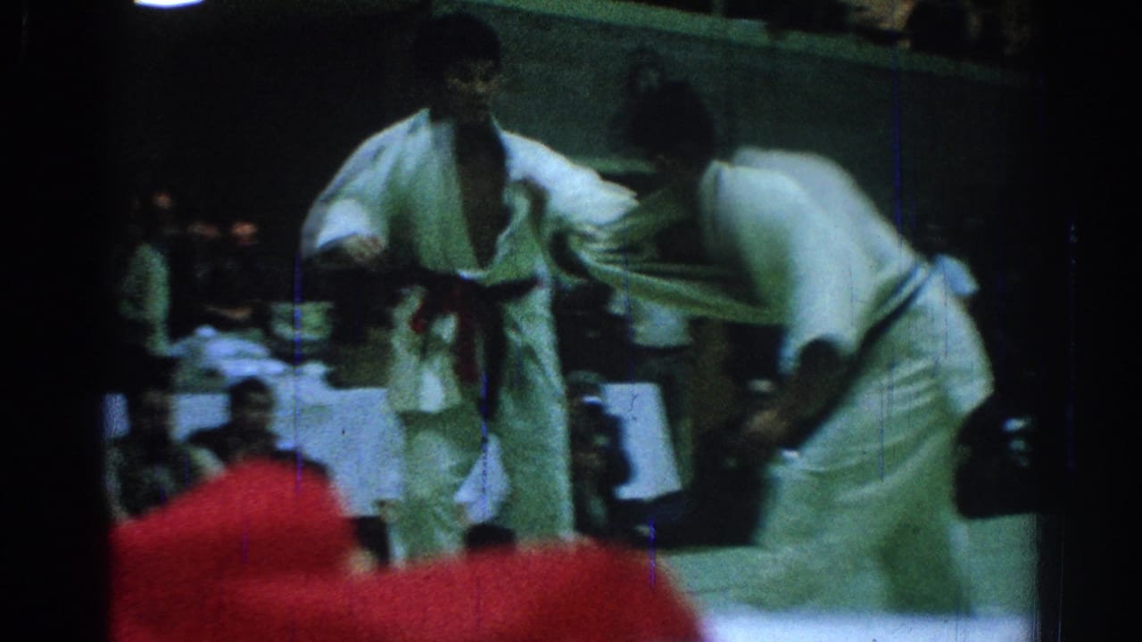 Two competitors in white gi grapple on a mat during a 1966 San Gabriel judo match, with spectators visible behind them.