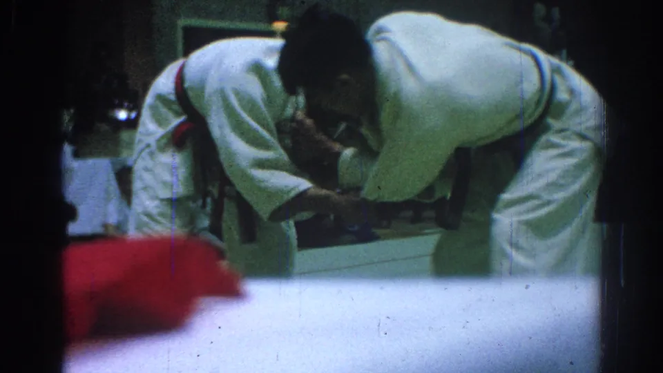 Two judo athletes in white gi lean into a close grip during the San Gabriel match, partly obscured by foreground blur and film wear.