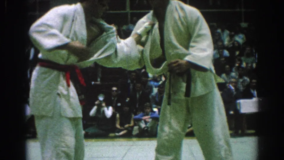 Two adult karate competitors in white gi and colored belts grapple on a mat in San Gabriel, California, in 1966.