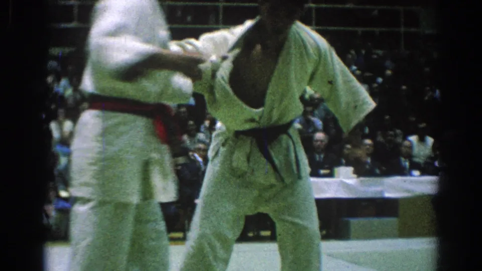 A black-belt competitor and a red-belt competitor hold close contact on the mat during the 1966 San Gabriel karate match.