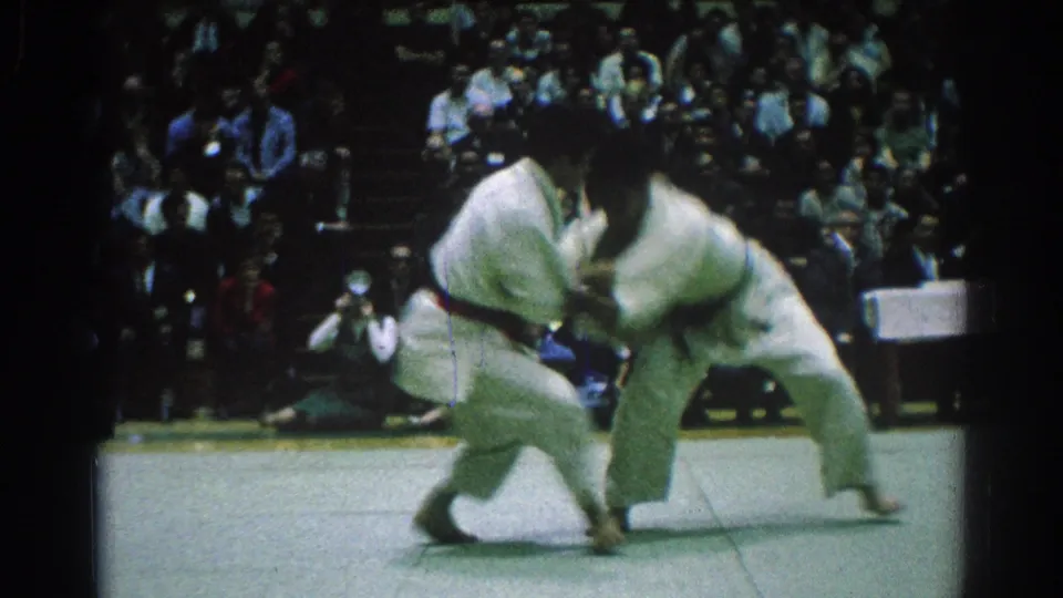During the San Gabriel judo match, one competitor leans over while the other moves low into a throw attempt on the mat.