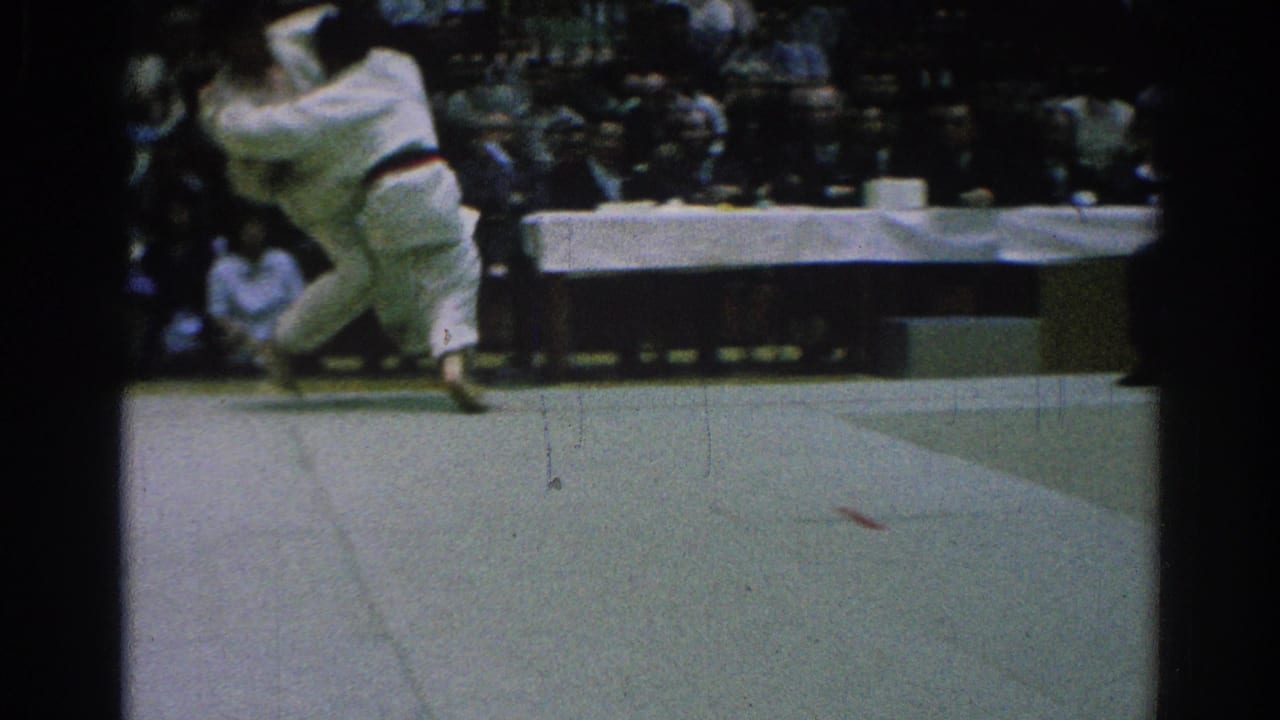 A judoka lifts or throws an opponent on the mat while spectators watch.