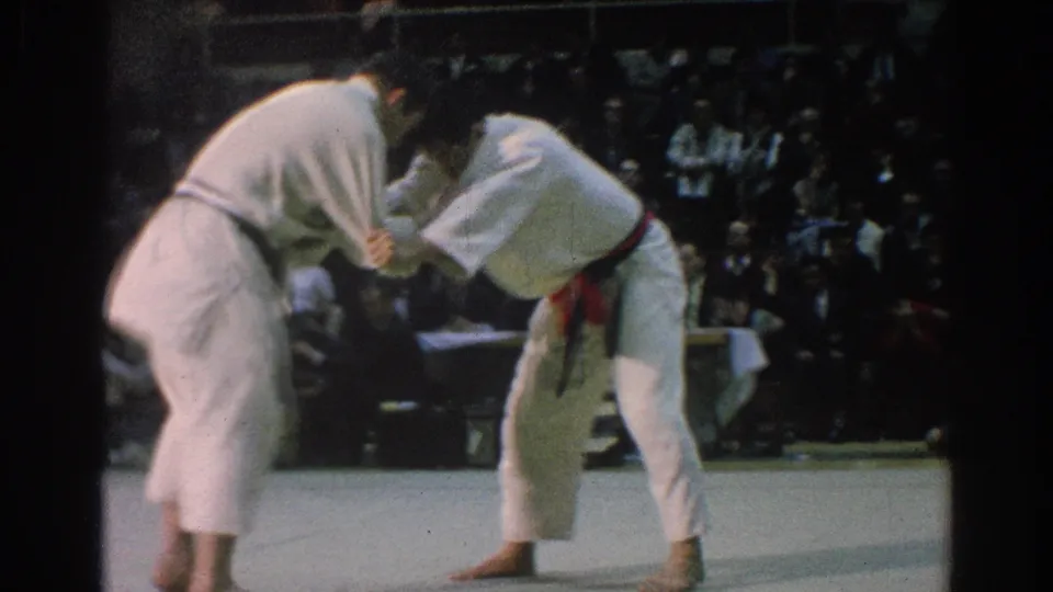 A 1966 karate match in San Gabriel shows two competitors maintaining a tense grip on the mat as the audience looks on.