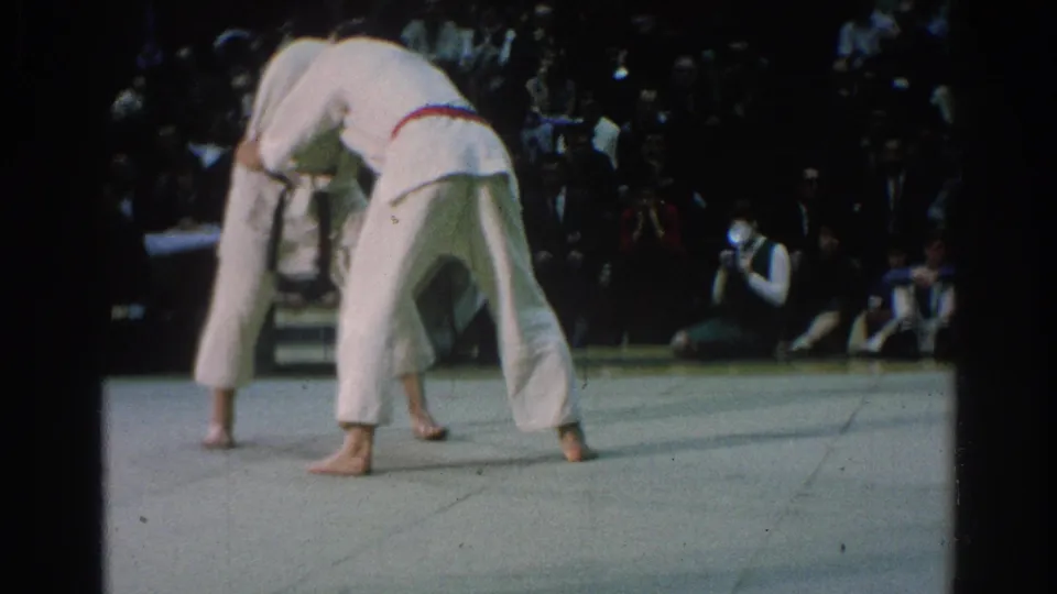 During the San Gabriel karate competition, the red-belt competitor bends low while the opponent presses in during a close exchange.