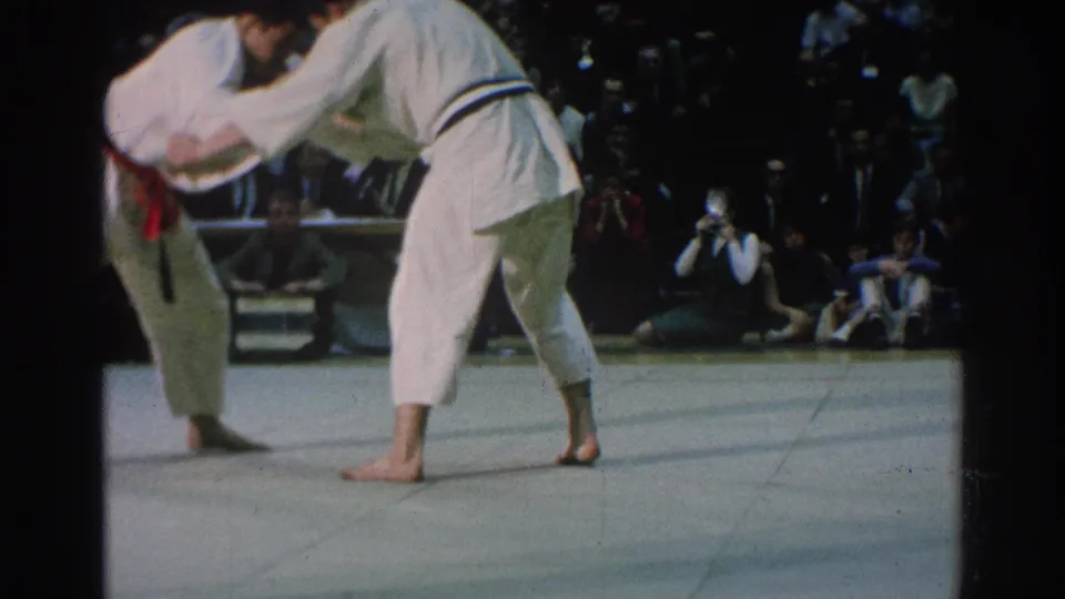 The 1966 San Gabriel footage shows two karate competitors still engaged on the mat as photographers and spectators watch closely.