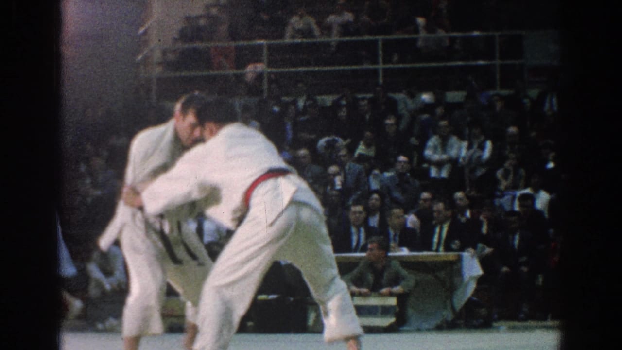 During the San Gabriel judo match, the red-belt competitor leans into a throw attempt as the opponent holds position.